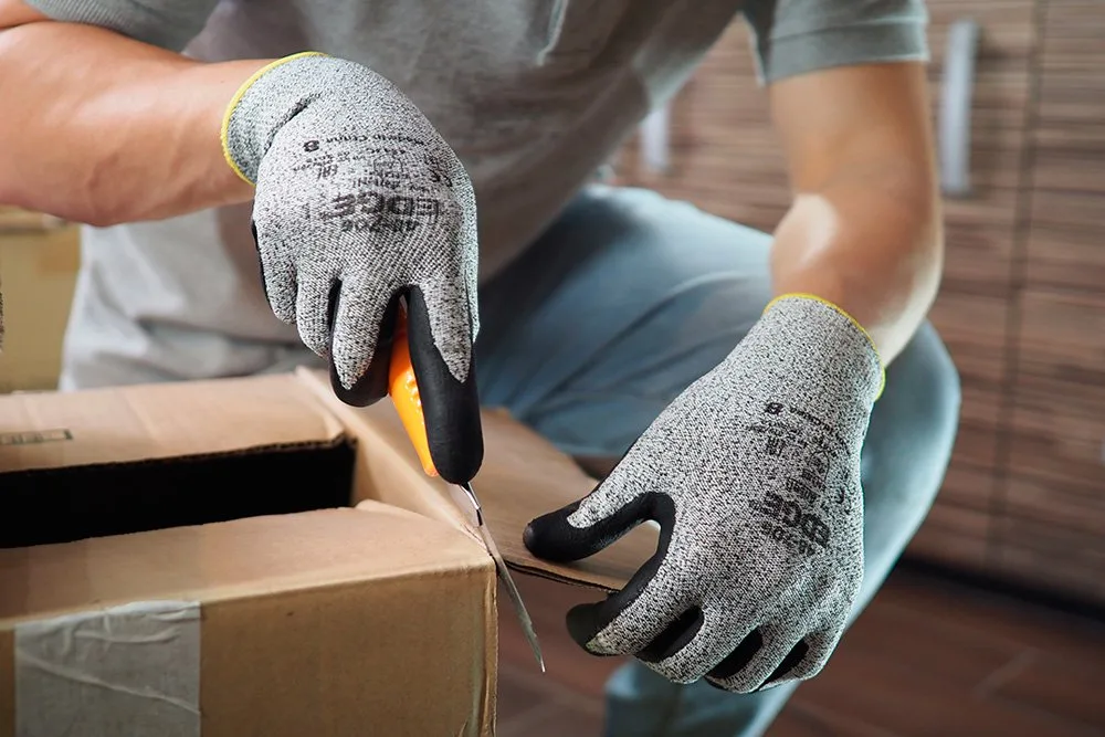 Trabajador con guantes anticorte abriendo una caja con cutter